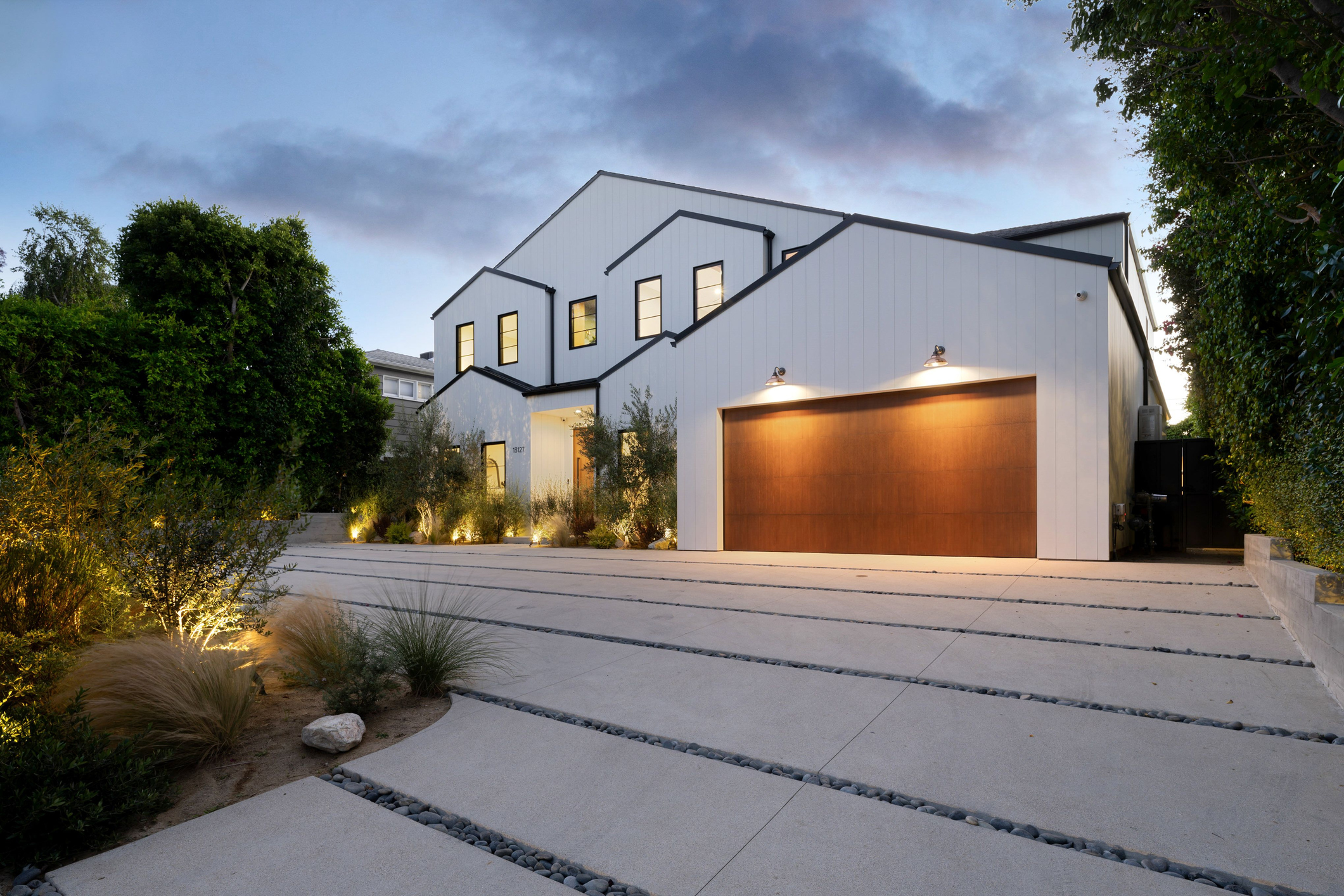Modern white house exterior with black window frames and wooden garage door.