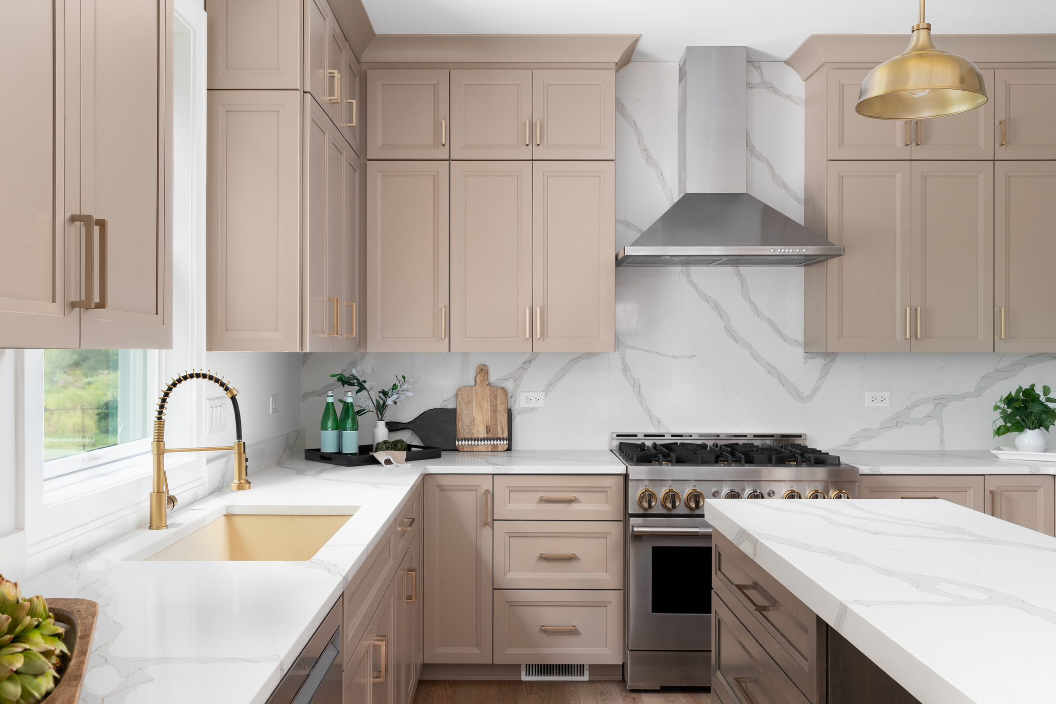 Close-up of taupe kitchen cabinets with gold handles and marble backsplash.